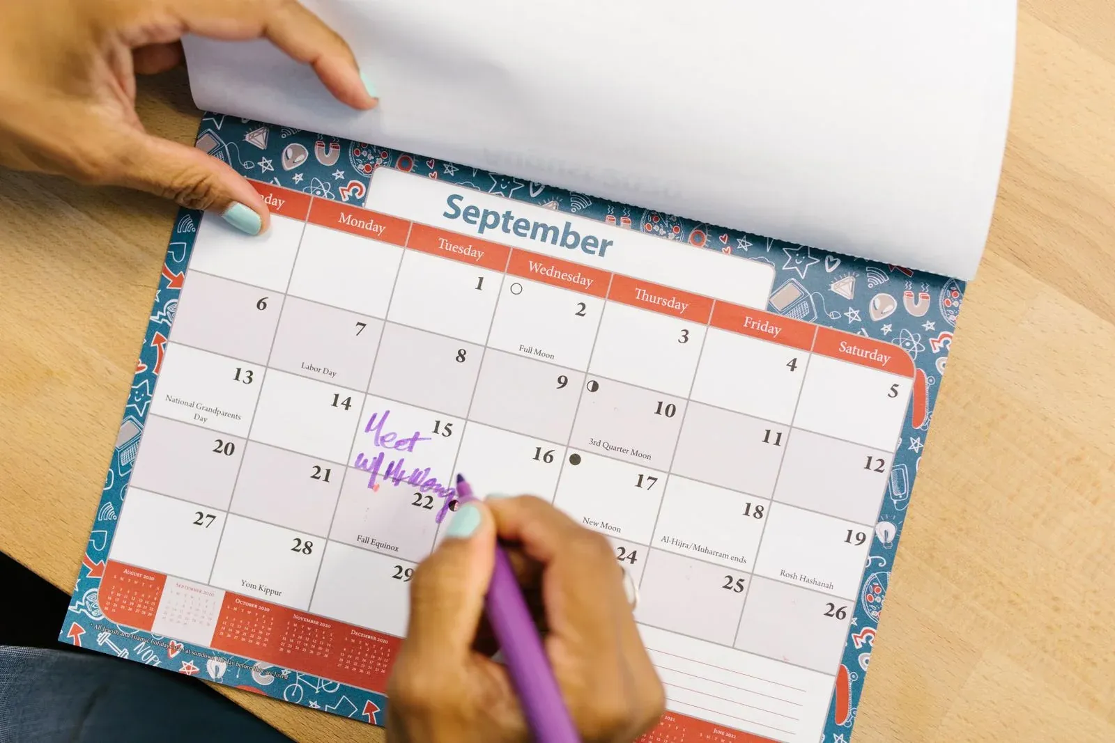 Des mains marquent des dates sur un calendrier posé sur un bureau en bois
